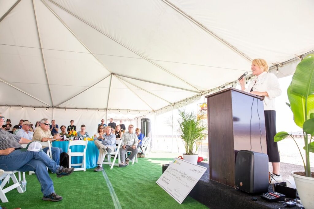 PCE's CEO Shawn Marshall speaks at a podium in front of a gathering of people underneath a white tent