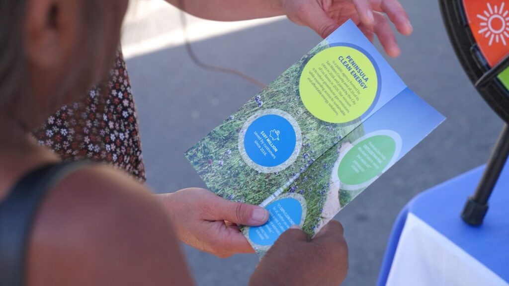 Close-up of a woman holding a PCE pamphlet in her hands while explaining it to a female community event attendee