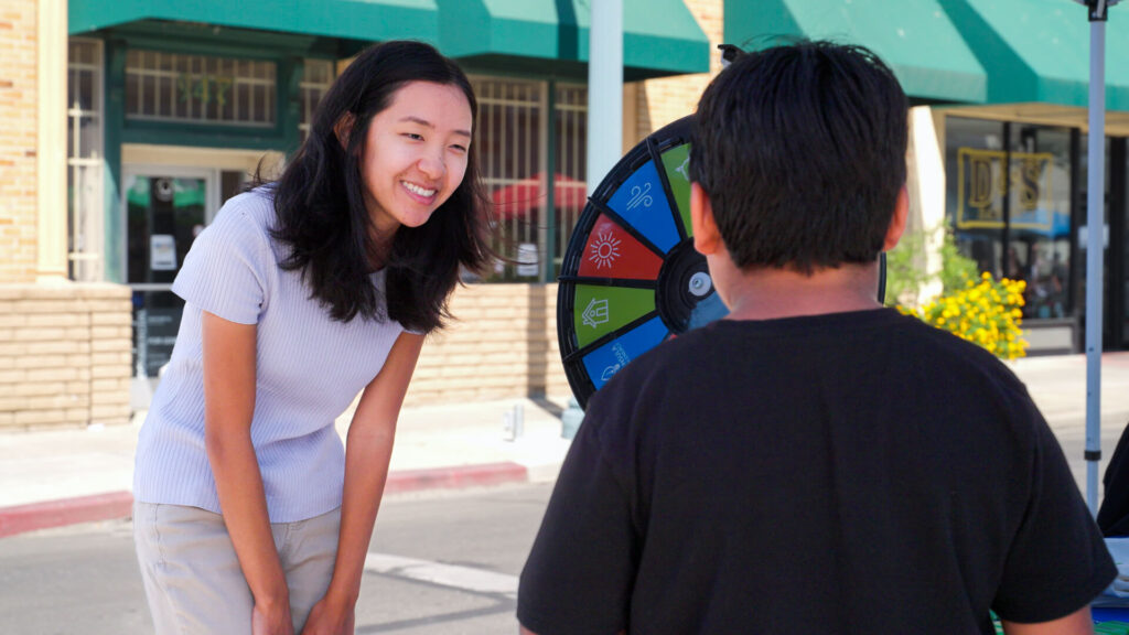 Vanessa Shin from Peninsula Clean Energy talking with a student about renewable energy at an educational event, featuring an interactive learning wheel.