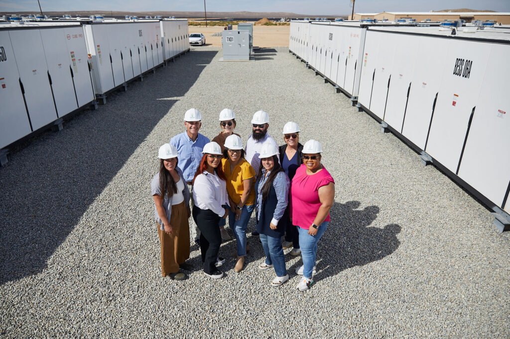 Group of Peninsula Clean Energy employees in hard hats standing in front of energy storage units, showcasing their commitment to 100% renewable power.