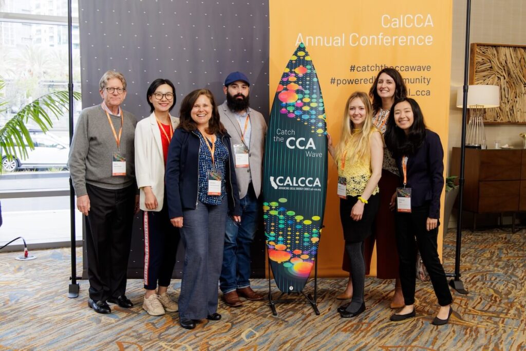 PCE staff members stand in front of a surfboard that reads "Catch the CCA Wave" at the CalCCA Annual Conference