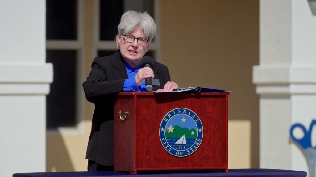 Brisbane Board member Coleen Mackin holds a microphone and speaks at a podium for the Mission Blue ribbon cutting