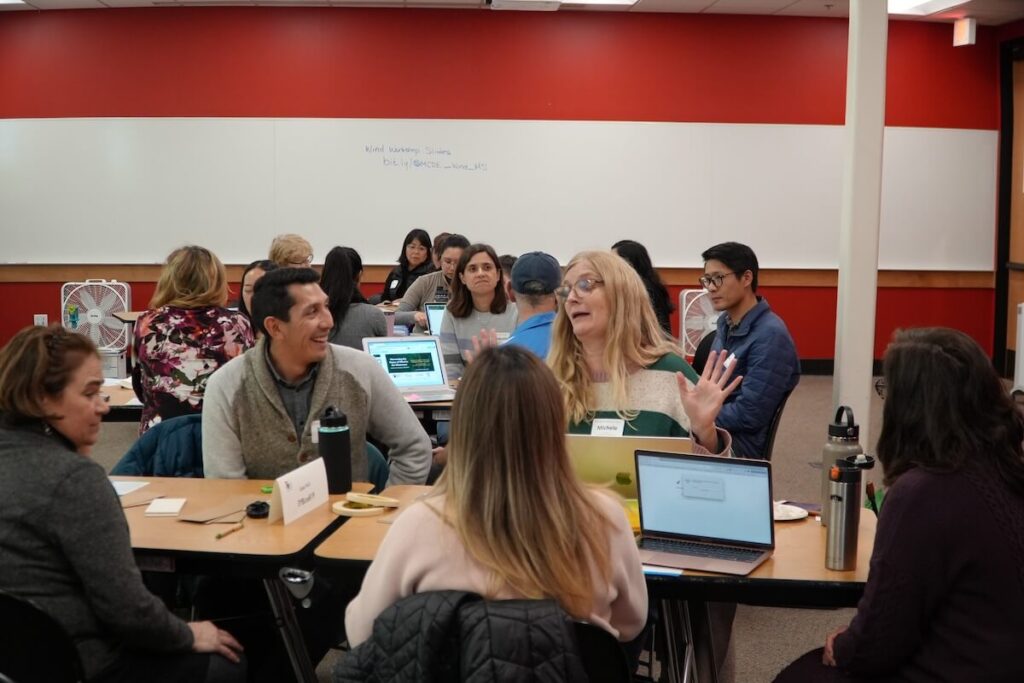 A large group of teachers sit at tables as they discuss an exercise about teaching students about wind power